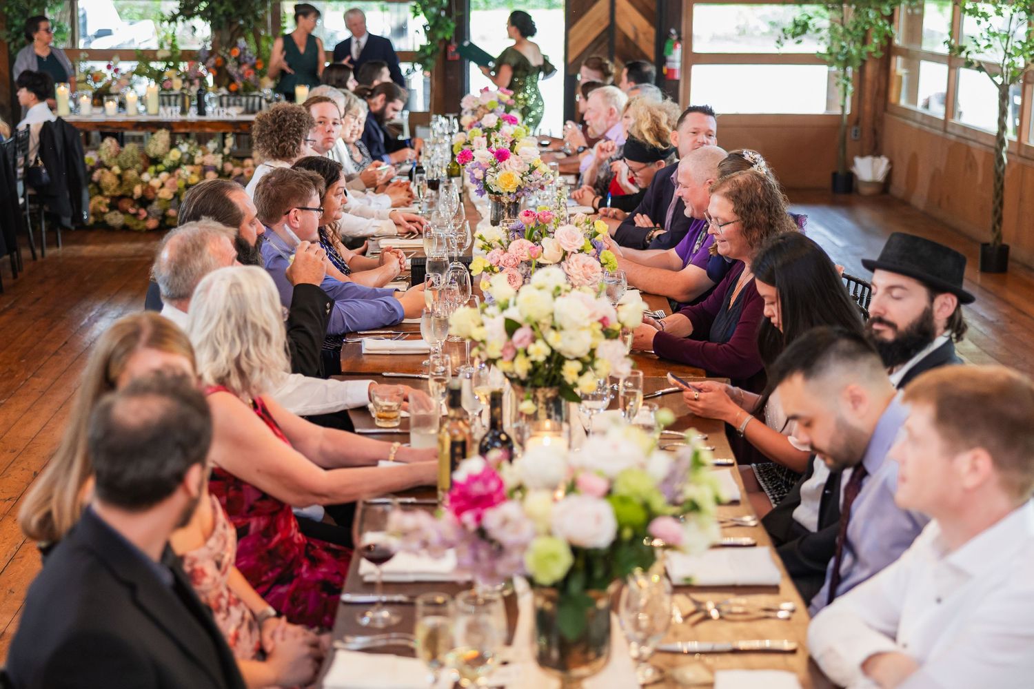 Guests seated at a long elegantly decorated wedding reception table with pink and white flowers.