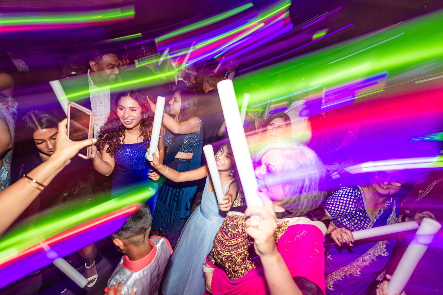 Colorful light trails illuminate a crowded nightclub dance floor with glowing party accessories.