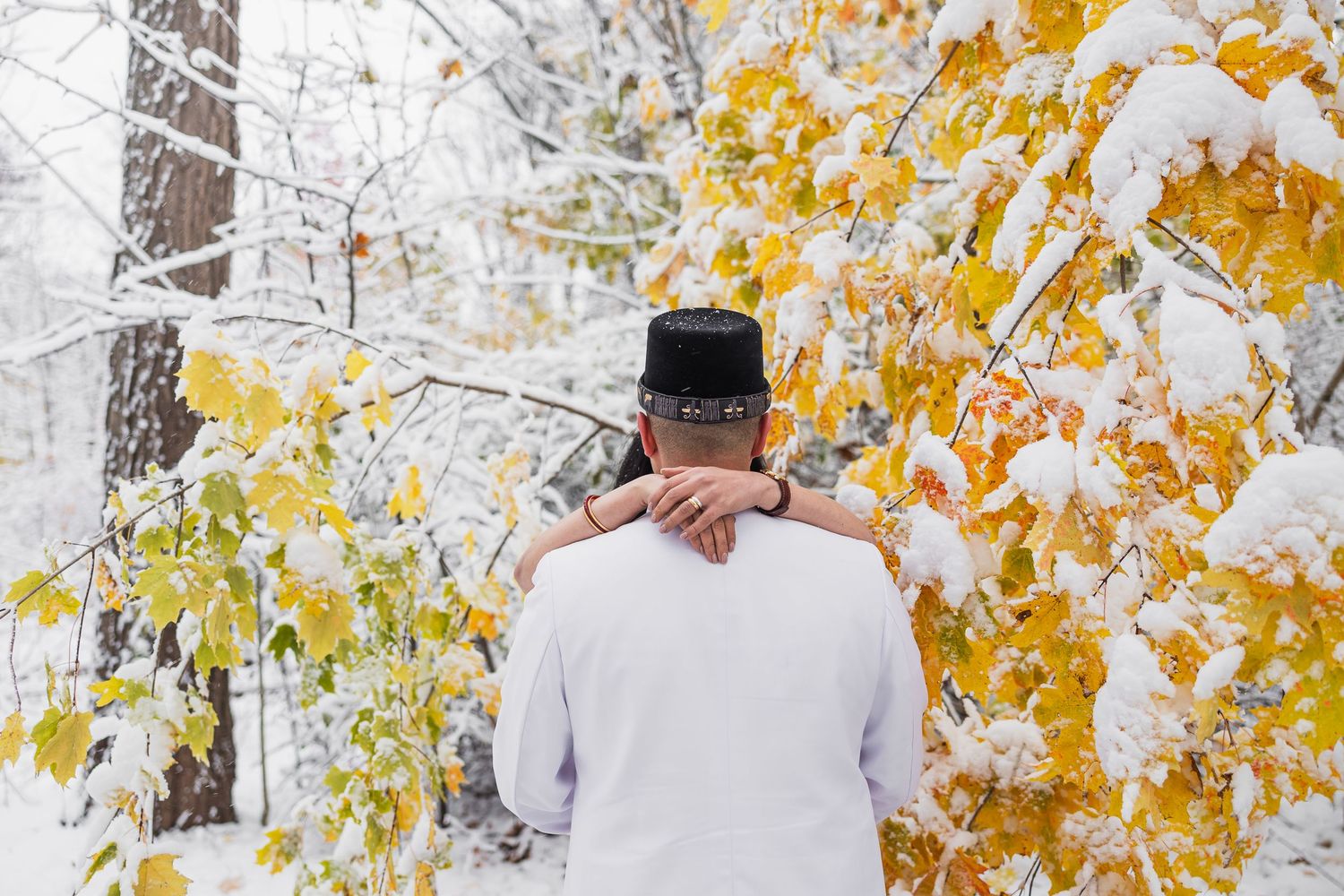 Couple walking through snowy woods with golden autumn leaves creating a romantic winter scene.