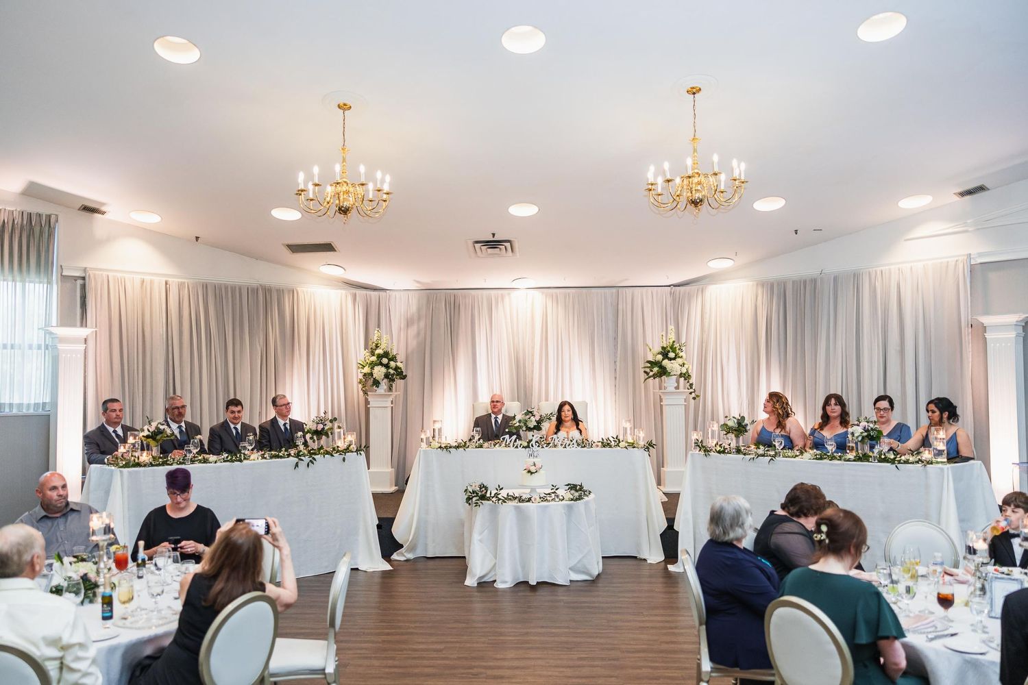Elegant wedding reception venue with white draping, chandeliers and guest tables.