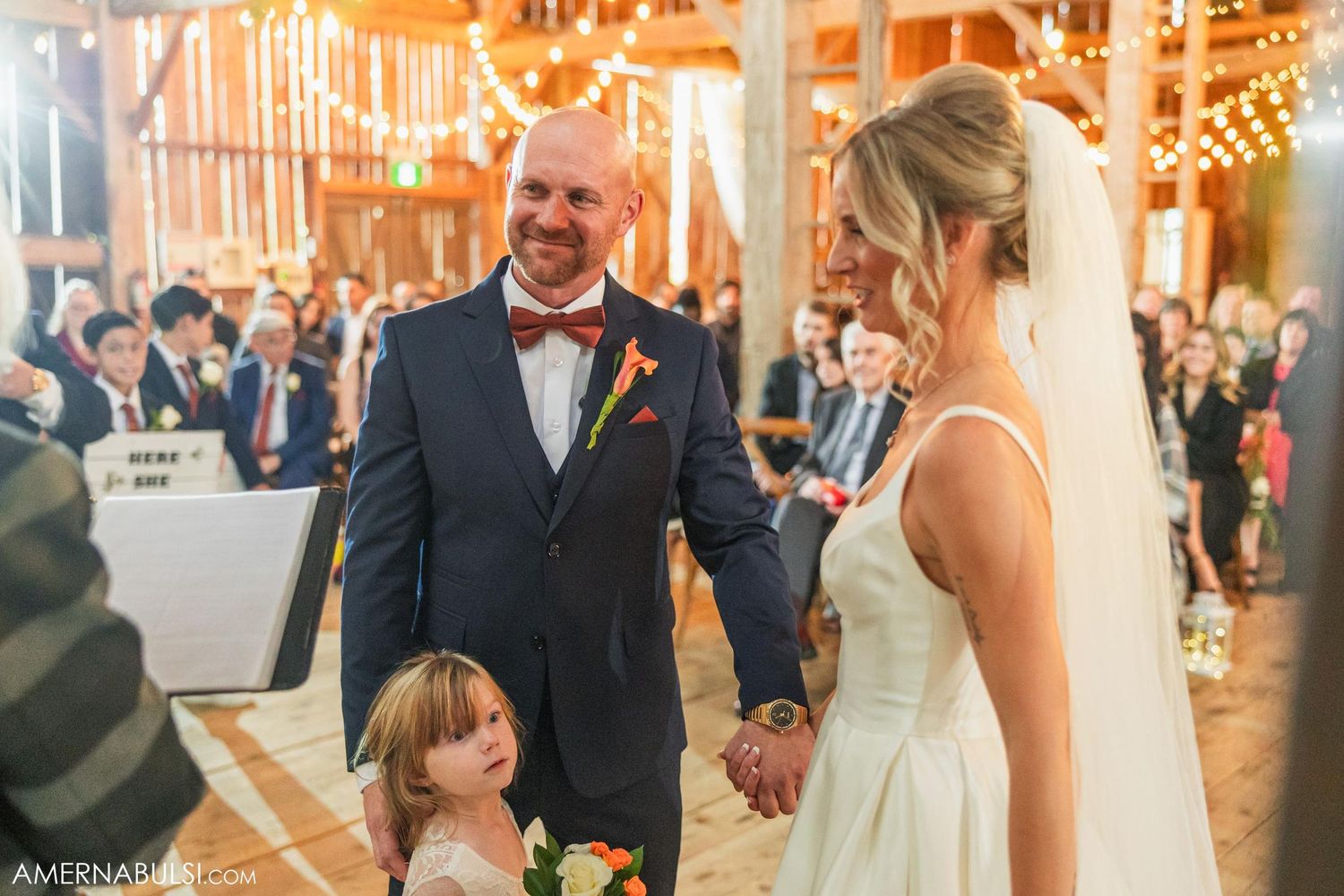 Intimate wedding ceremony moment in a rustic wood barn with string lights and elegant decorations.