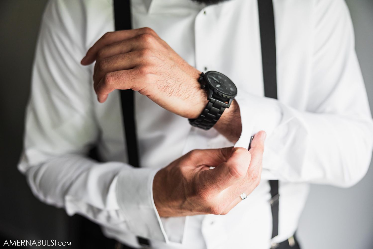 Close up of hands adjusting watch while wearing white shirt and black suspenders.