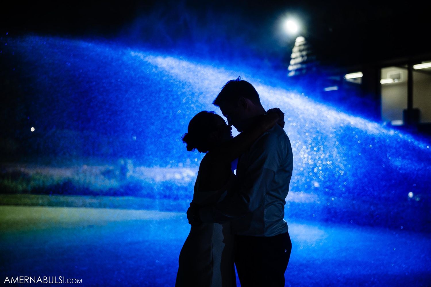 Silhouetted couple embraces under dramatic blue lighting in nighttime setting.