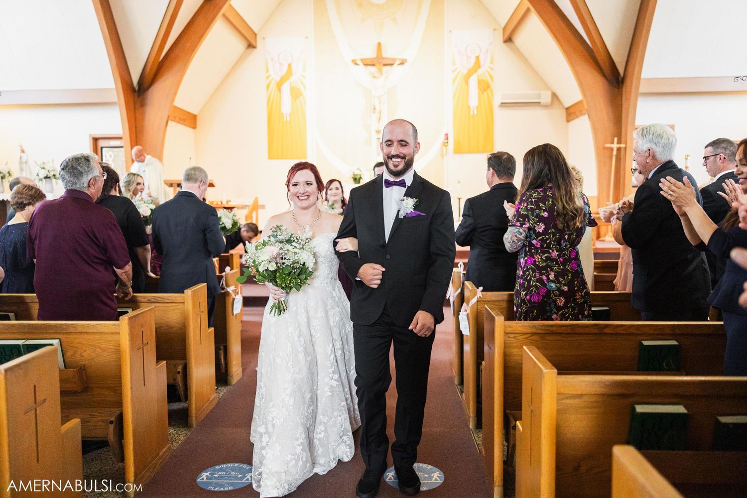 Newlyweds exit down the aisle of a traditional church with exposed wooden beams.