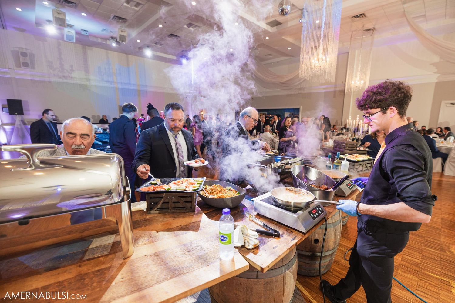 Catering staff prepares food at wedding reception buffet with rising steam.