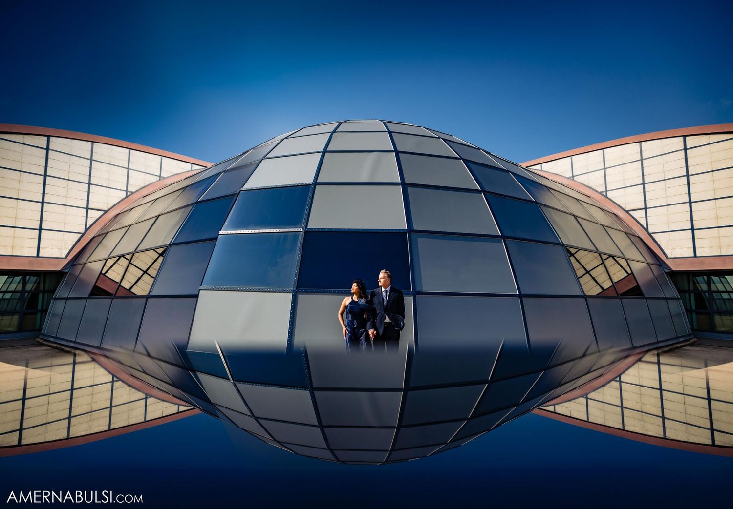 A couple poses in an artistic reflection shot against a modern dome structure.