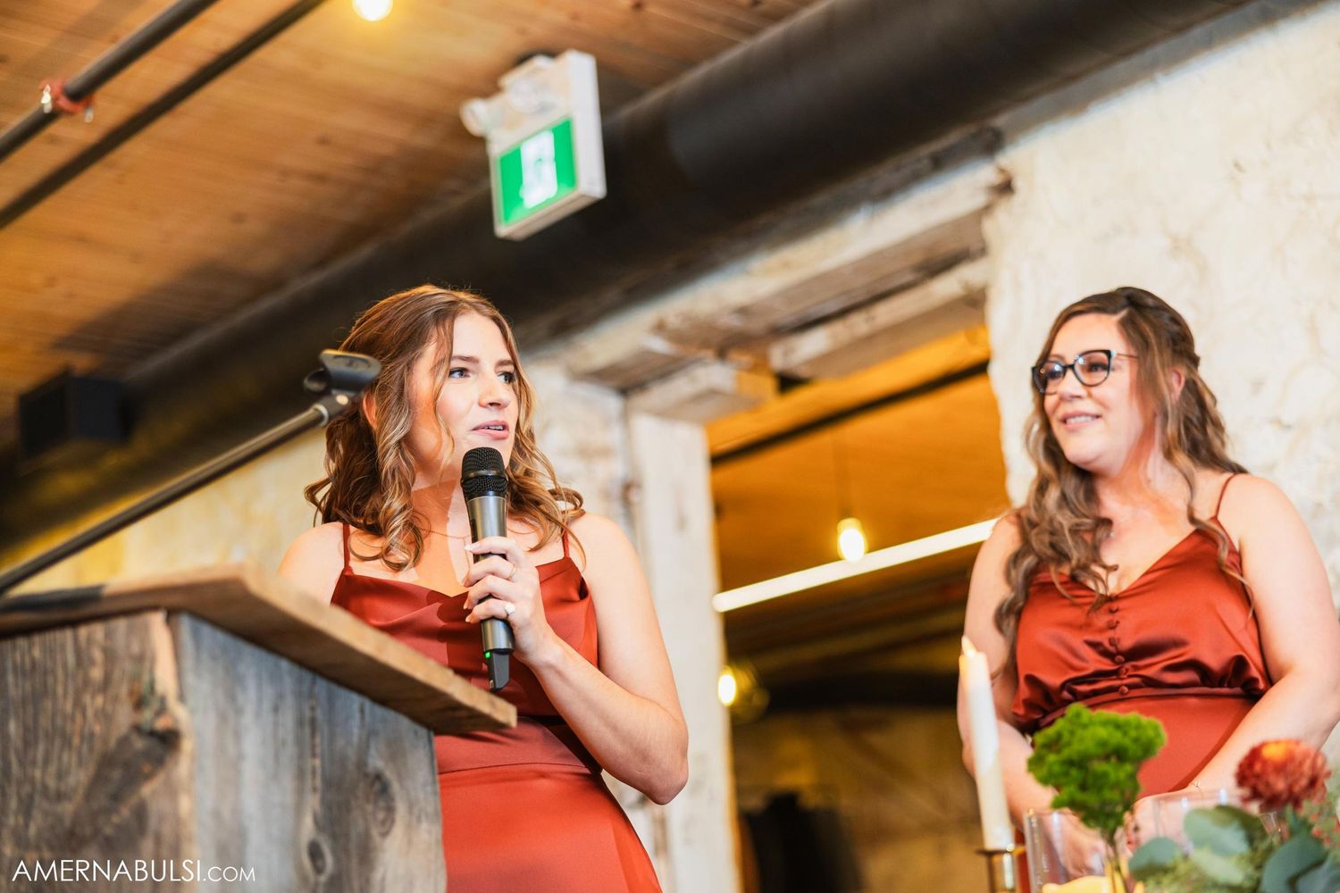 Two women in red dresses giving speeches at a celebration event.