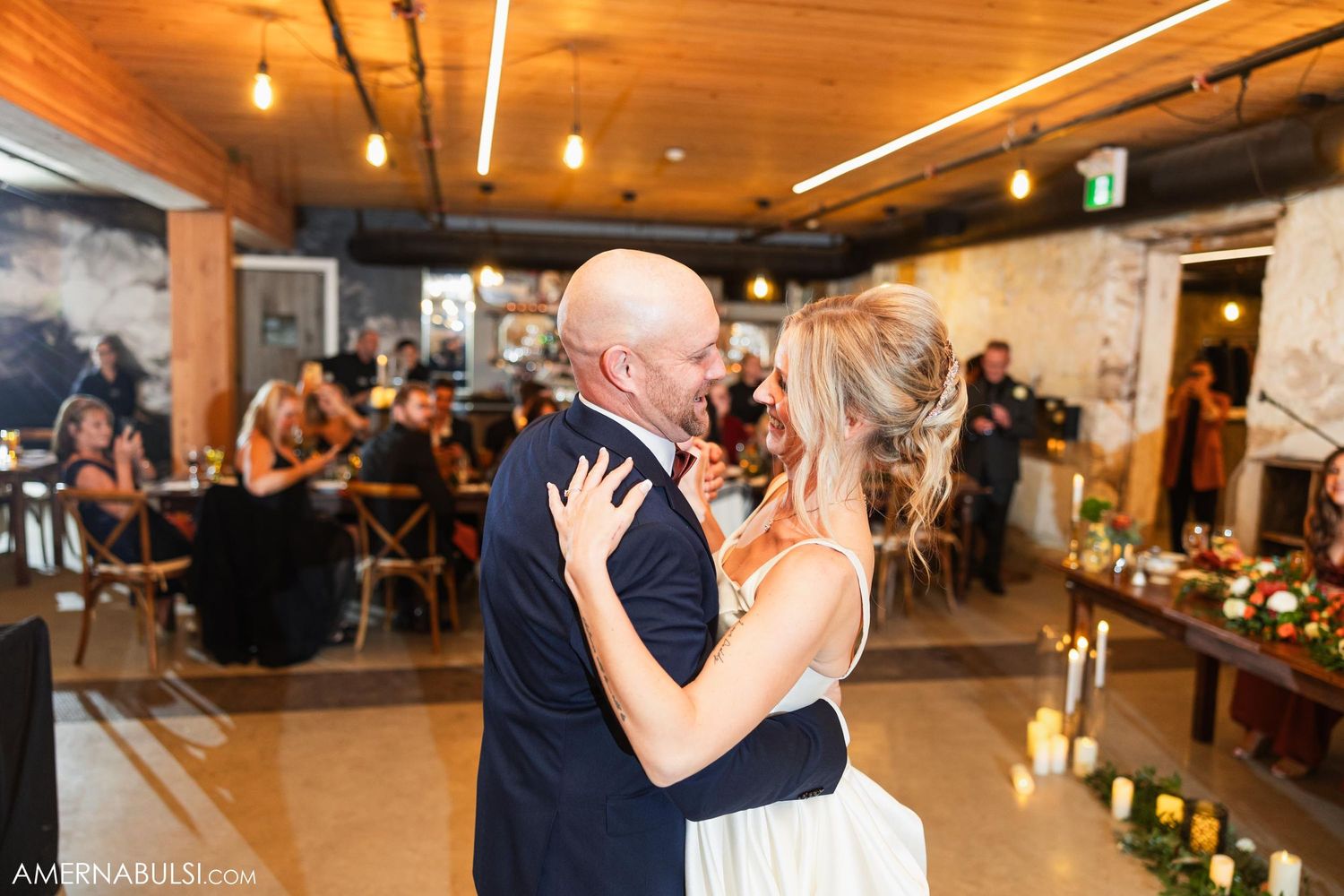 Newlyweds share intimate slow dance during wedding reception in industrial venue.
