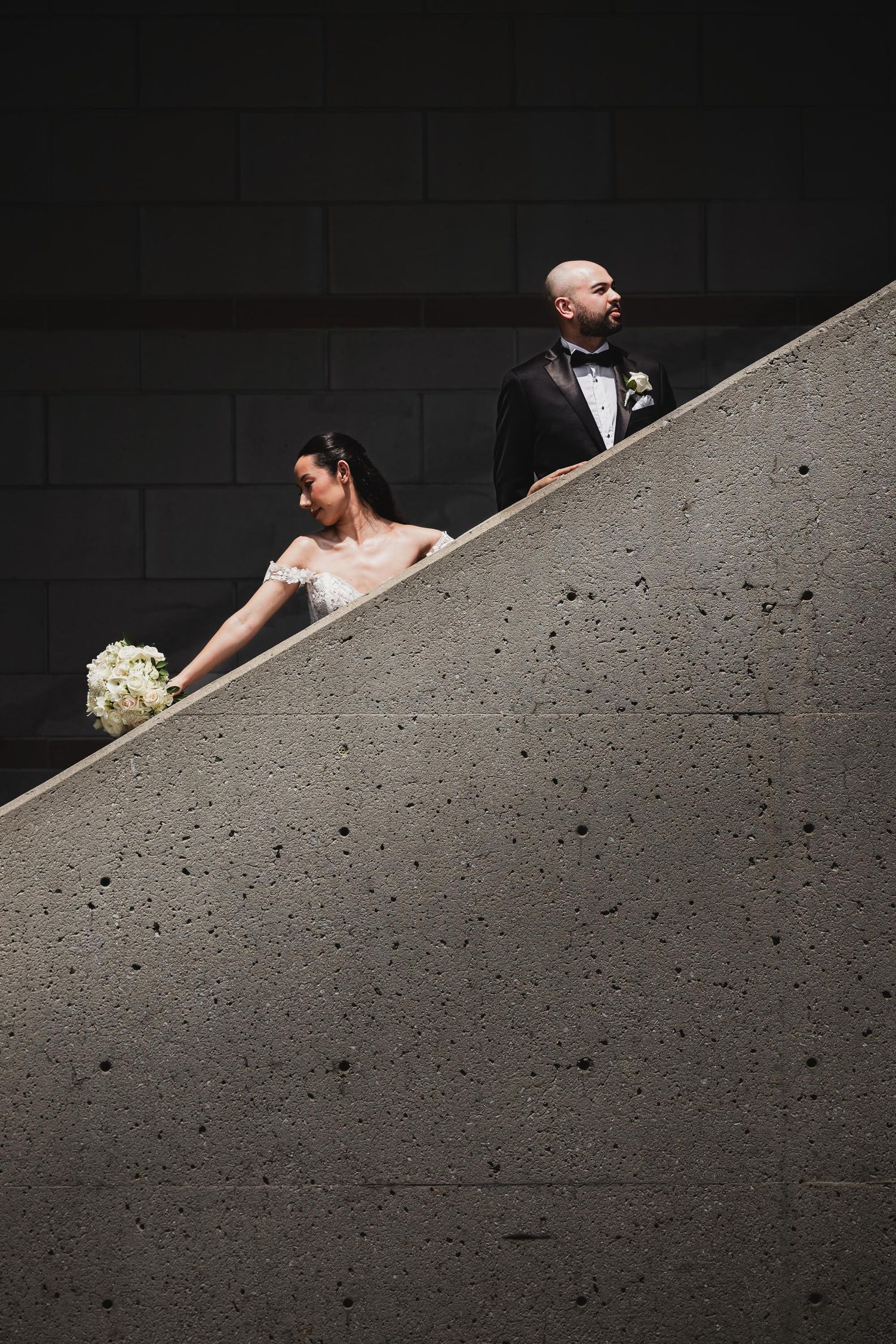 Wedding couple posed on concrete stairs in artistic black and white composition.