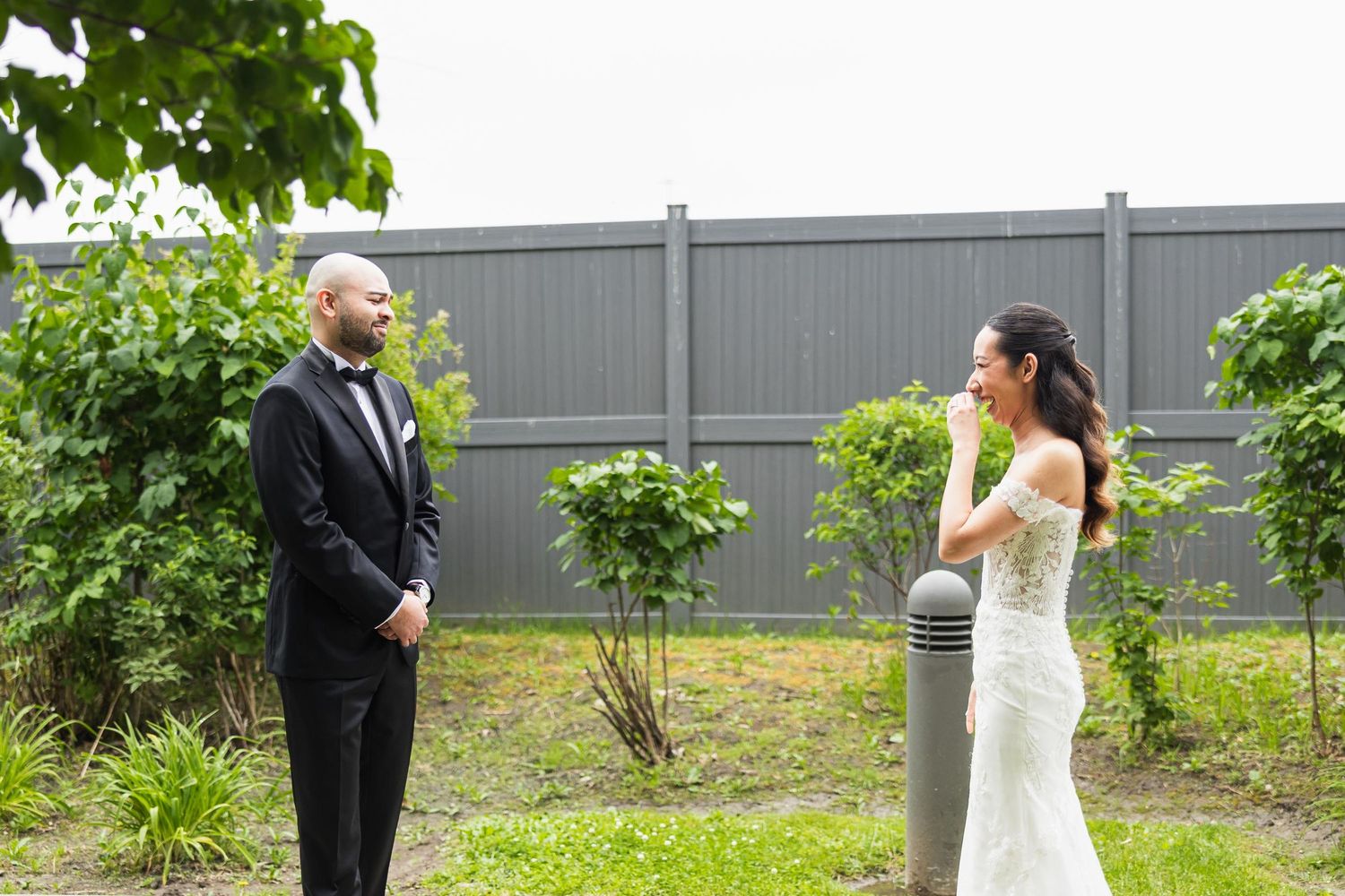 A wedding couple standing apart during their first look in a garden setting.