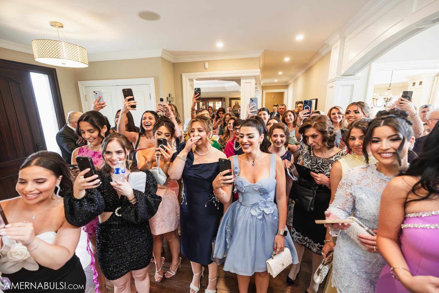 Wedding guests gathered in a bright indoor space taking photos and celebrating.