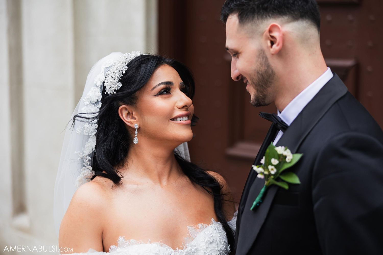 Newlyweds share an intimate moment showcasing bride's elegant veil and groom's boutonniere detail.