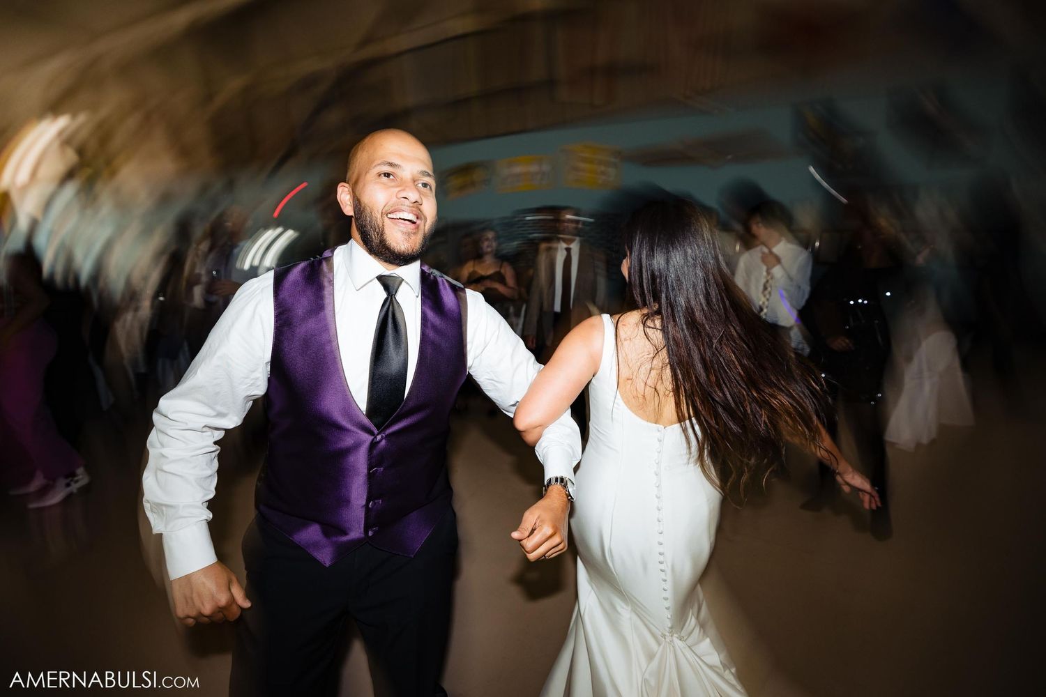Bride and groom dancing energetically at their wedding reception with motion blur effects.