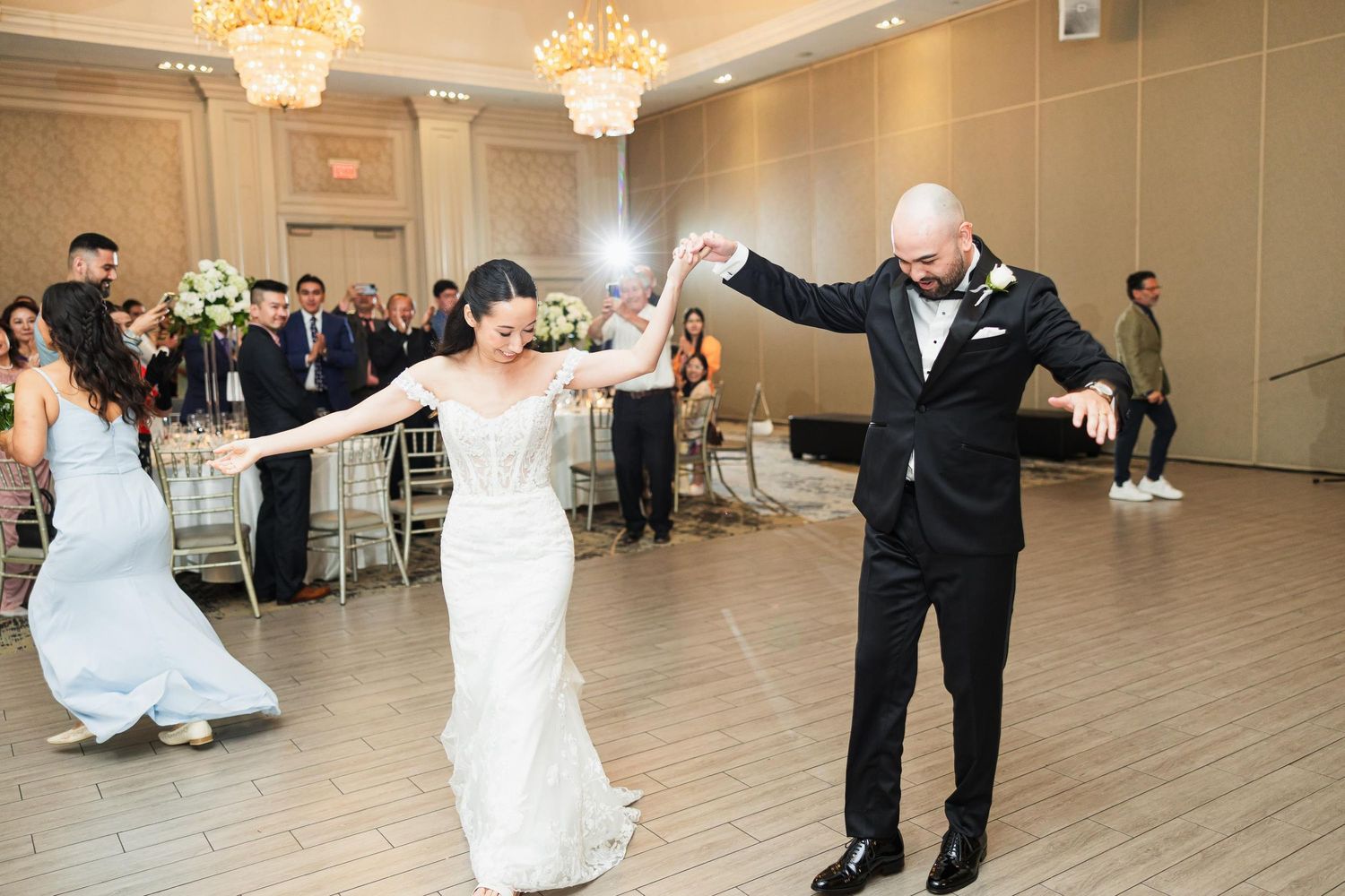 Couple shares their first dance in elegant ballroom with crystal chandeliers.