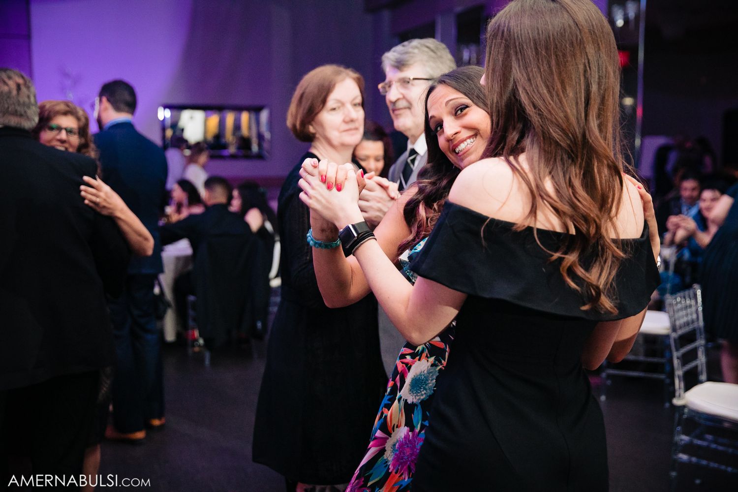 Couples dancing and celebrating on a dimly lit dance floor with purple ambient lighting.