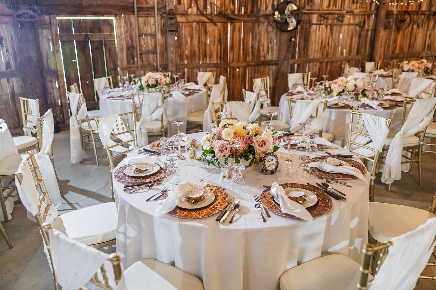 Rustic barn wedding reception venue with white linens and floral centerpieces on round tables.