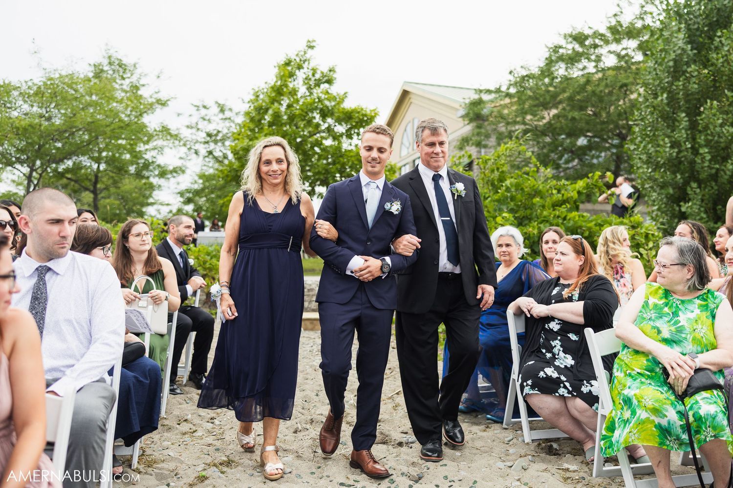 Wedding guests mingling on a lawn with a house in the background on a sunny day.