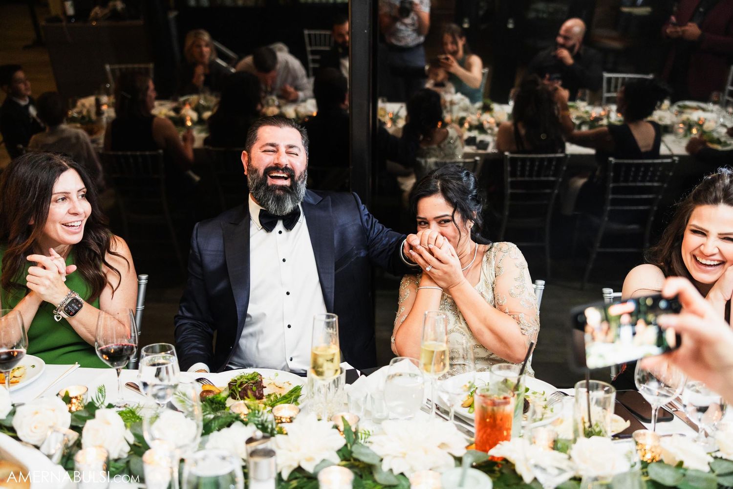 Joyful wedding reception moment with guests laughing at decorated dinner table.
