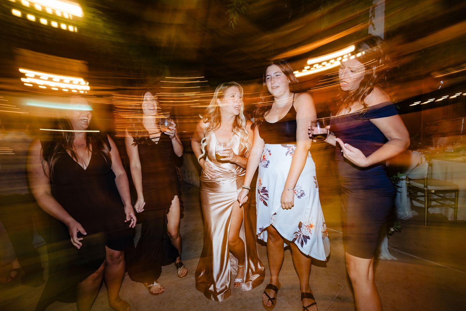 Wedding reception guests dancing together in a dimly lit rustic venue with warm lighting and festive atmosphere.