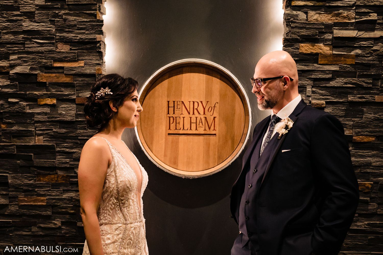 A couple stands in front of a wooden barrel display at Henry & Belle.