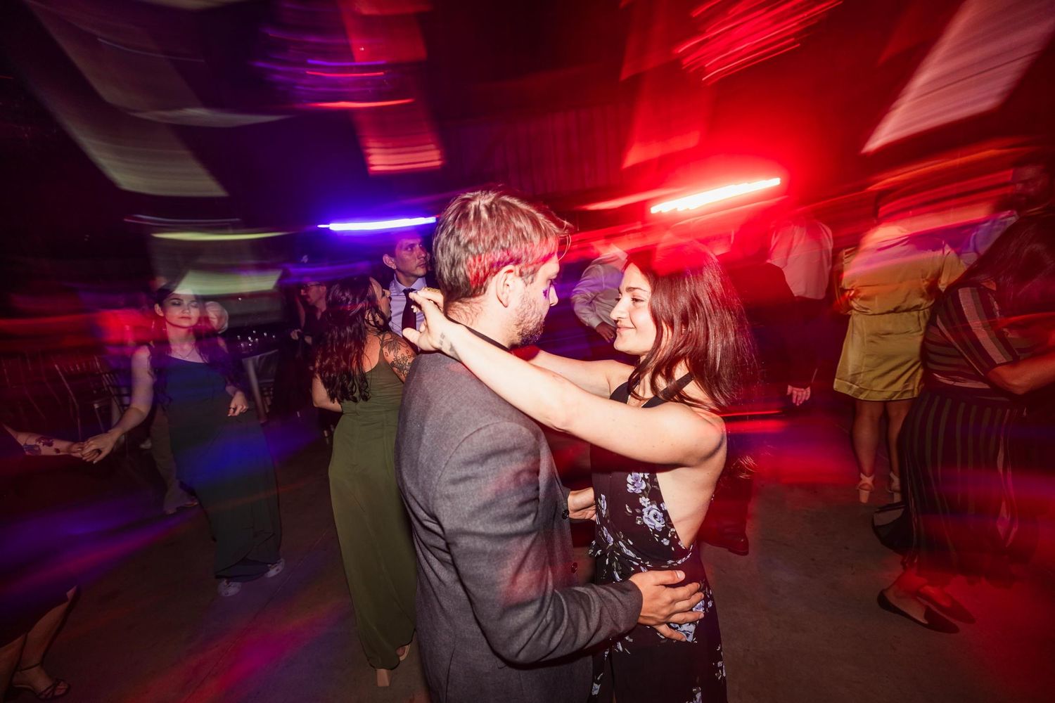 Couple slow dancing together under dramatic red lighting at wedding reception.