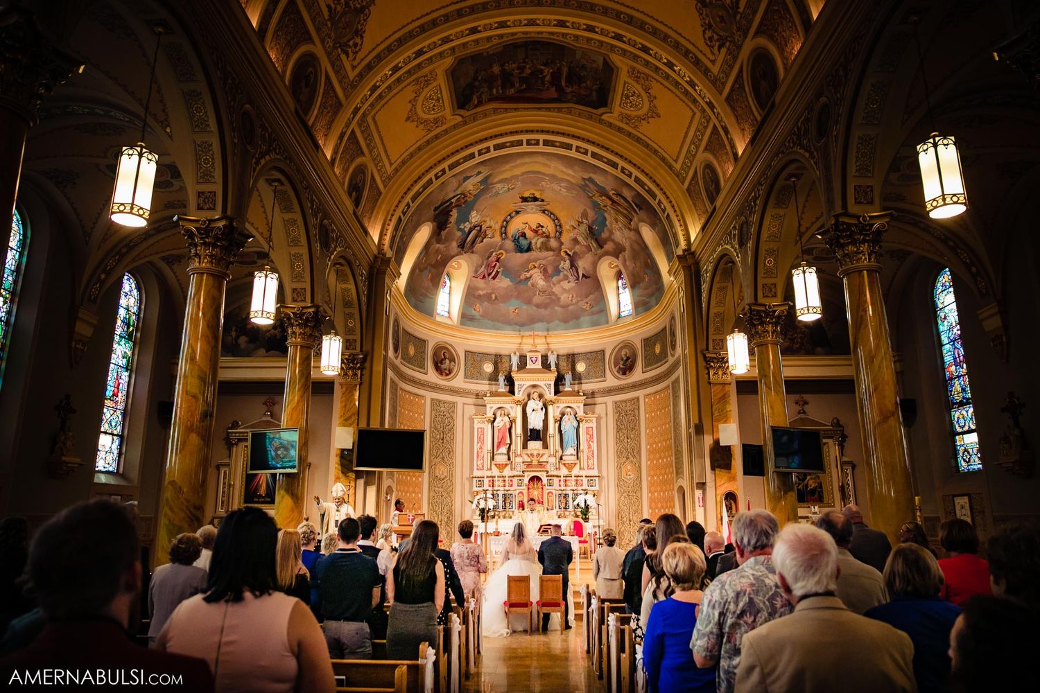 Ornate Catholic church interior with golden arches and painted ceilings illuminated by hanging pendant lights.