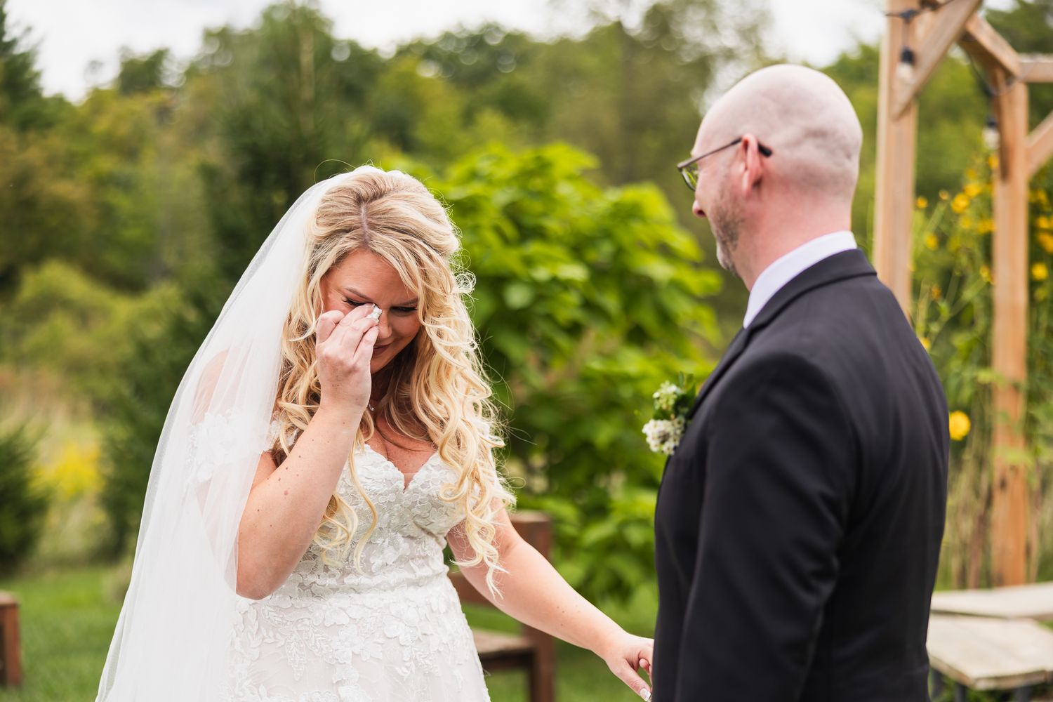 Wedding couple shares an emotional first look moment in a sunny garden setting with wooden pergola.