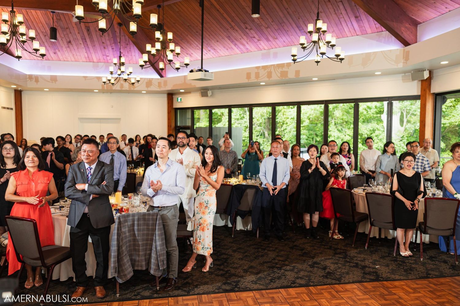 Large group of wedding guests gathered in an elegant reception venue with wood beam ceiling.