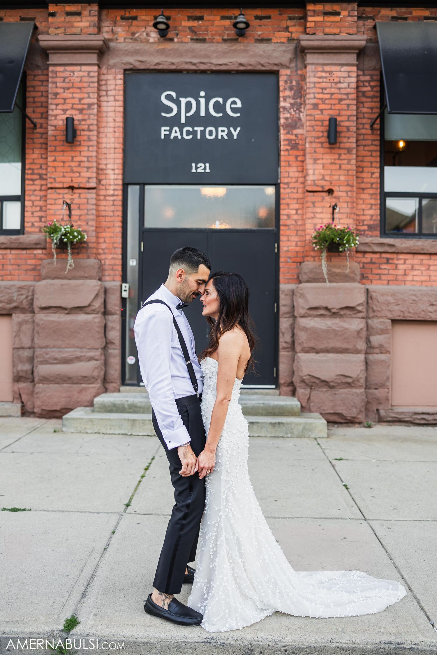 A wedding couple embraces in front of the Spice Factory brick building entrance.