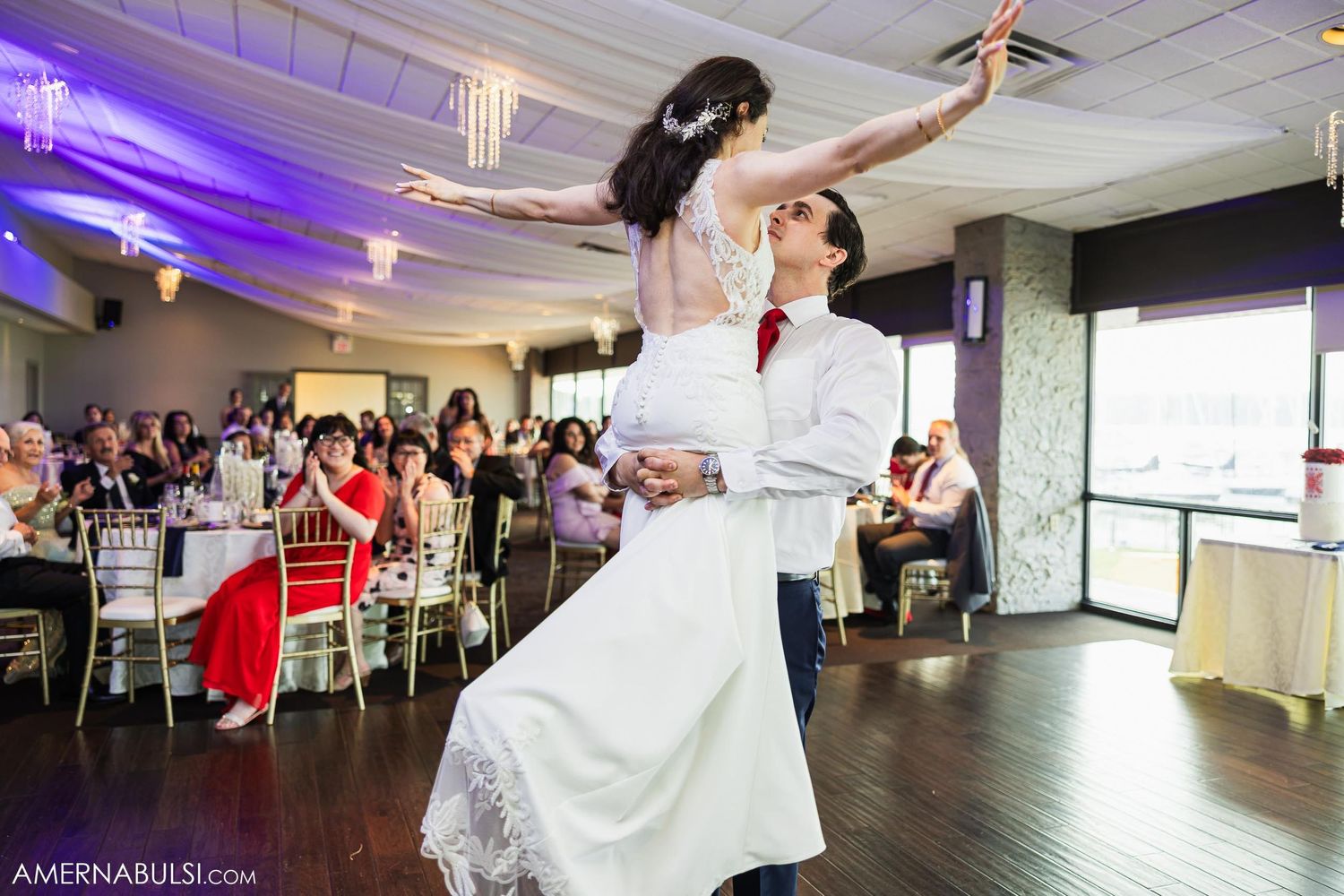 Couple dancing together during wedding reception in venue with purple lighting.