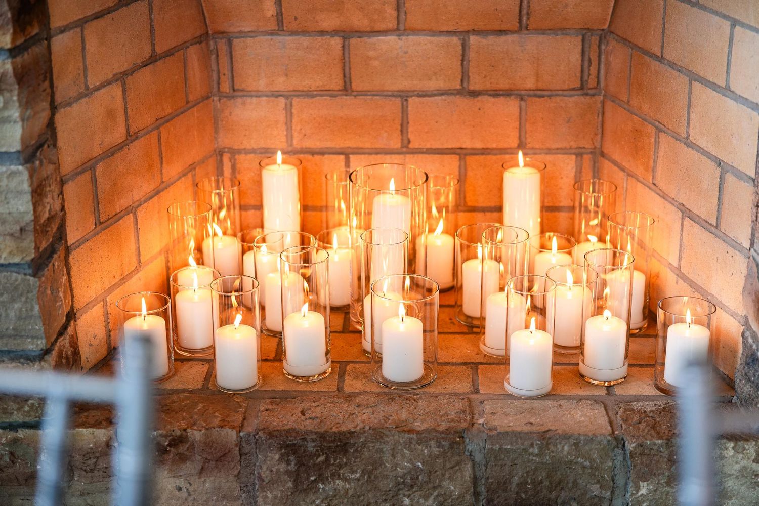 Array of glowing white candles arranged in rustic brick fireplace setting.