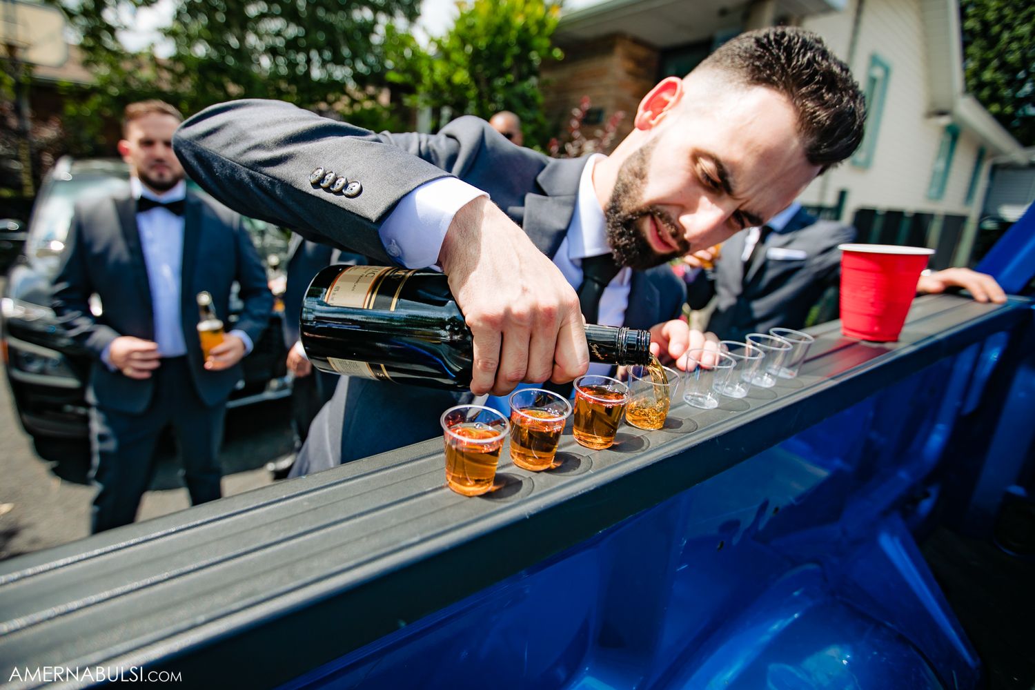 Multiple hands holding shot glasses in a toast formation against a blue tablecloth background.