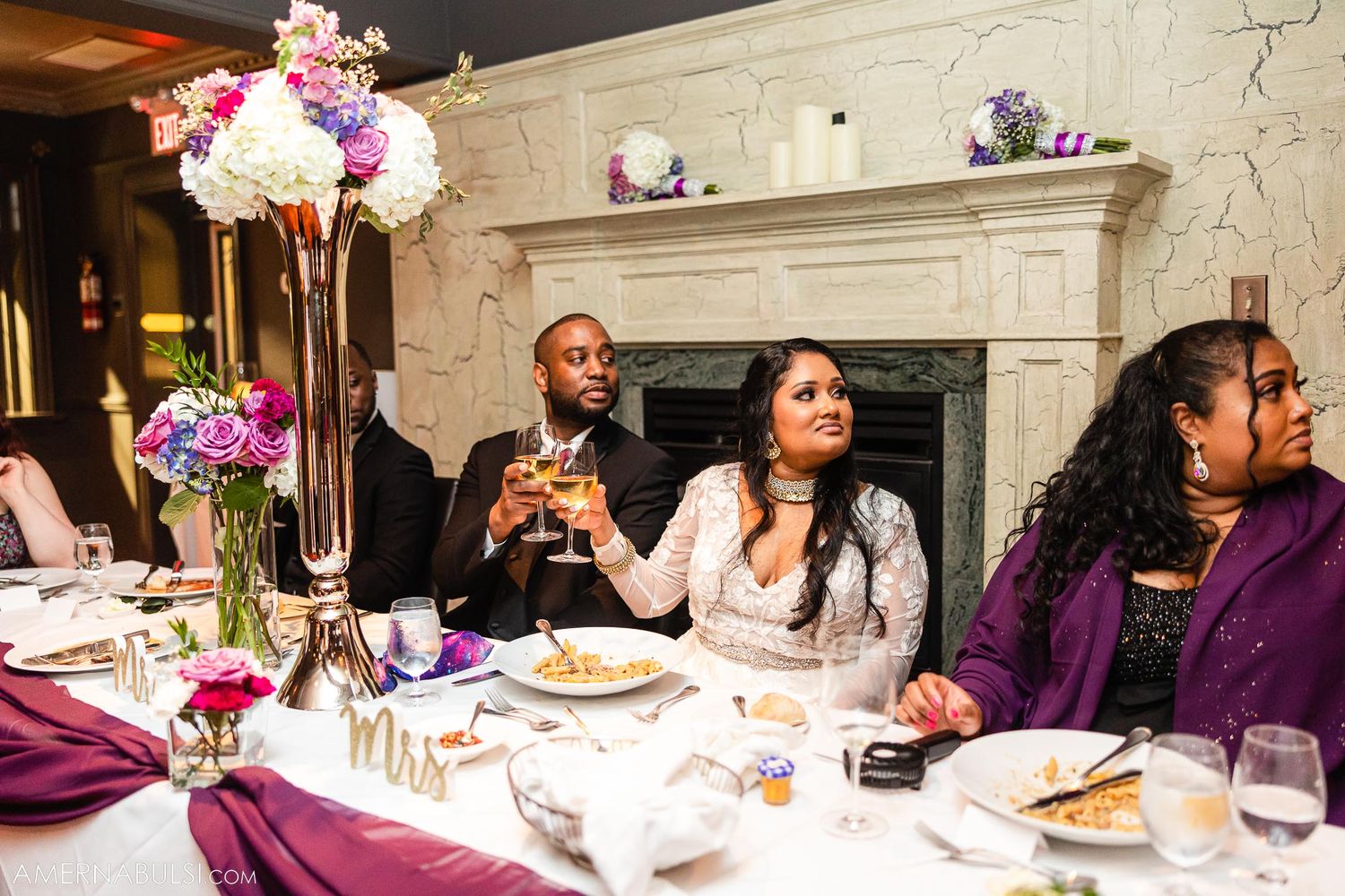 Wedding reception dinner table with purple decor, floral centerpiece and guests enjoying their meal.