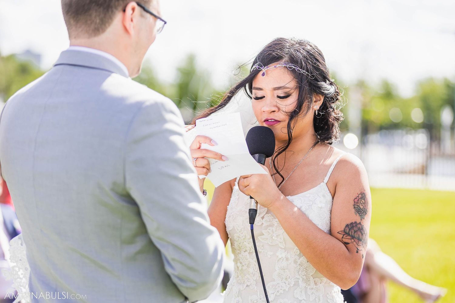 Bride speaks into microphone during outdoor wedding ceremony.