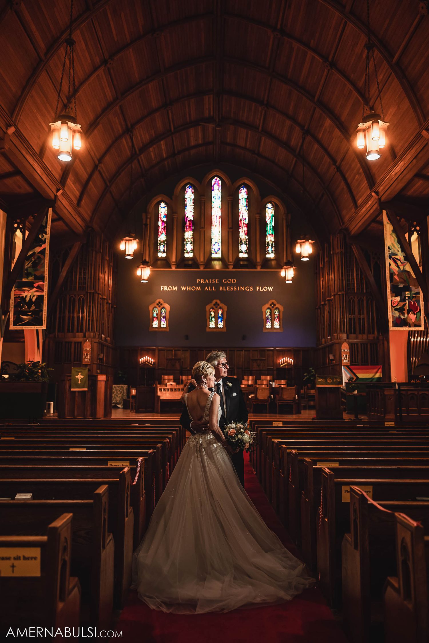 A dramatic church interior with stained glass windows and wooden arches frames a wedding scene.