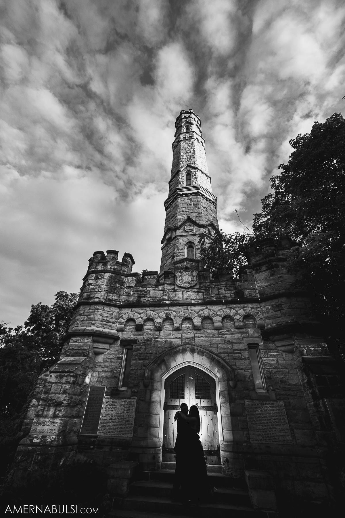Dramatic black and white photo of a silhouette against a gothic stone tower and cloudy sky.