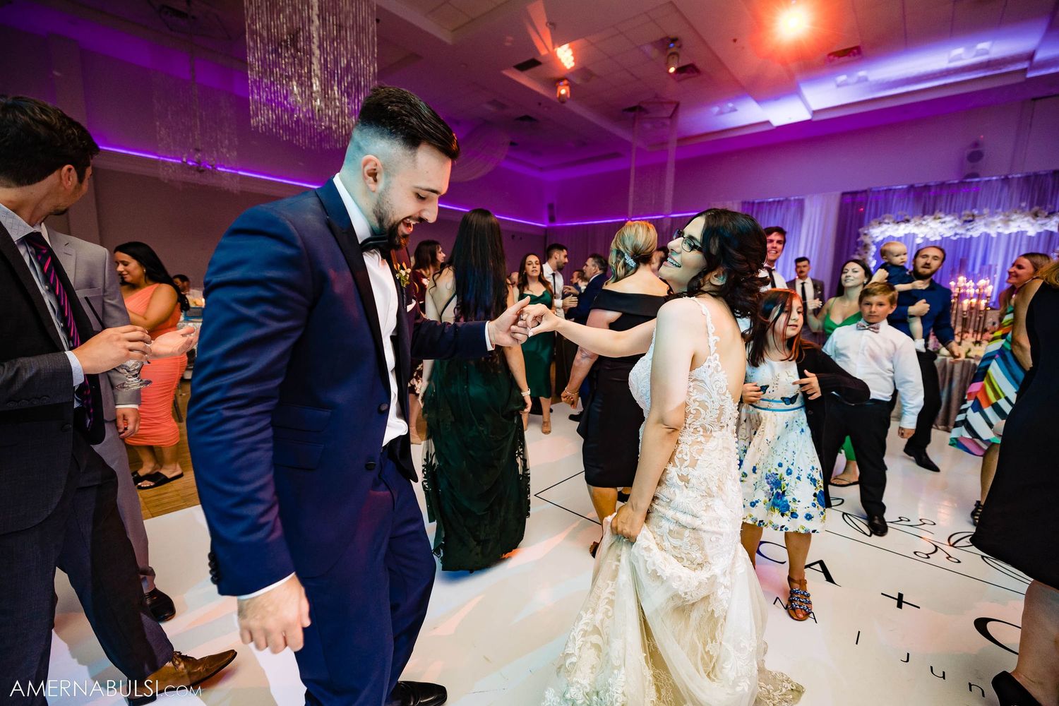Guests dancing at a wedding reception with purple lighting and elegant decor.