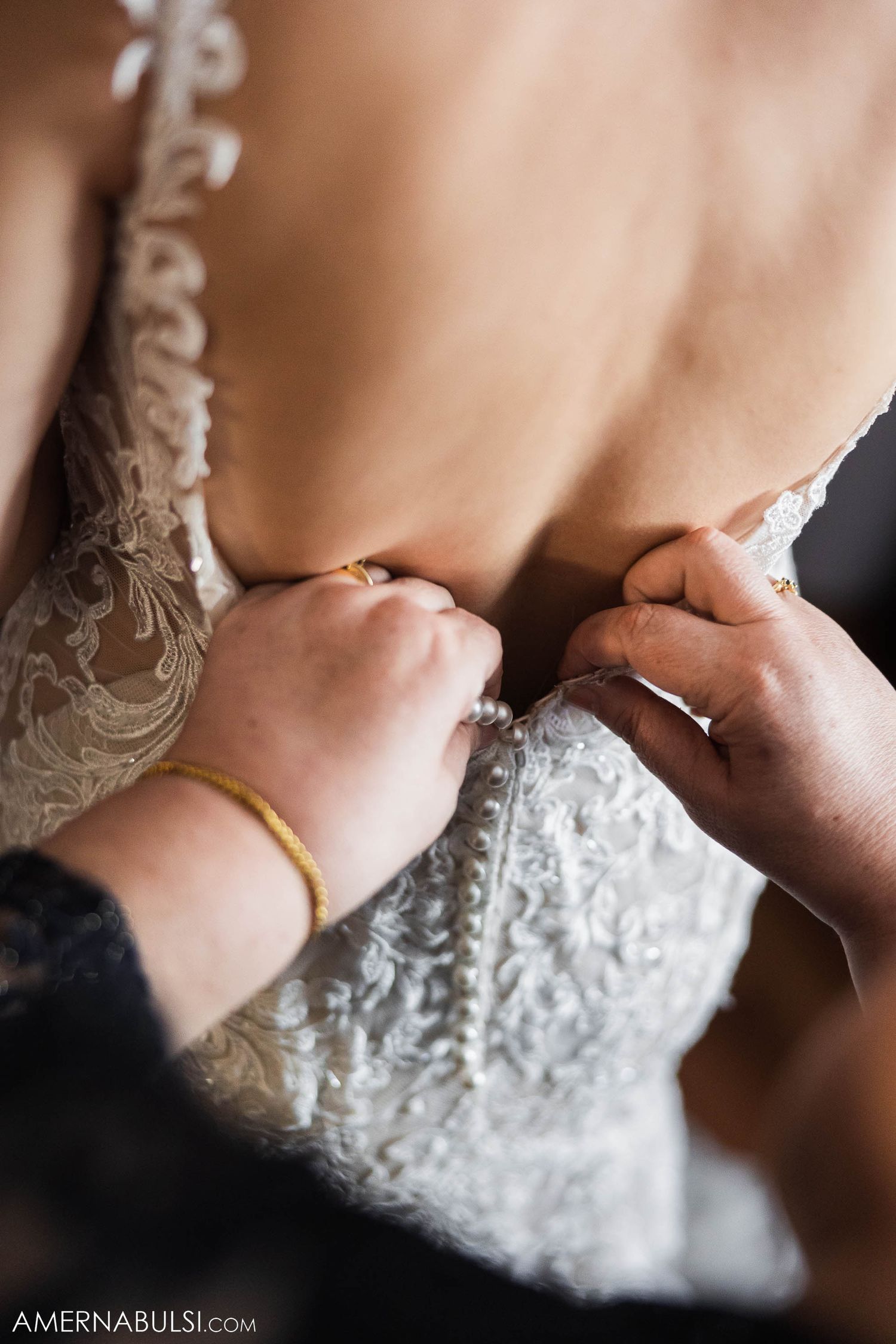 Close-up detail of intricate lace being buttoned on a white wedding gown.