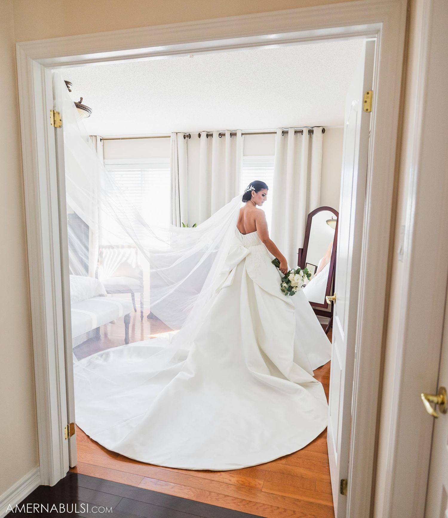 A dramatic view of a flowing white wedding gown with long train through a doorway.