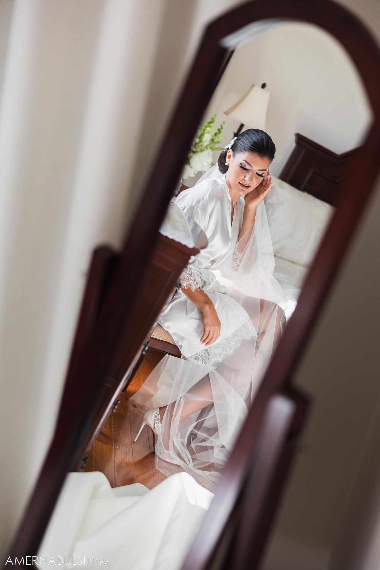 Getting ready scene reflected in arched mirror with flowing white fabric.