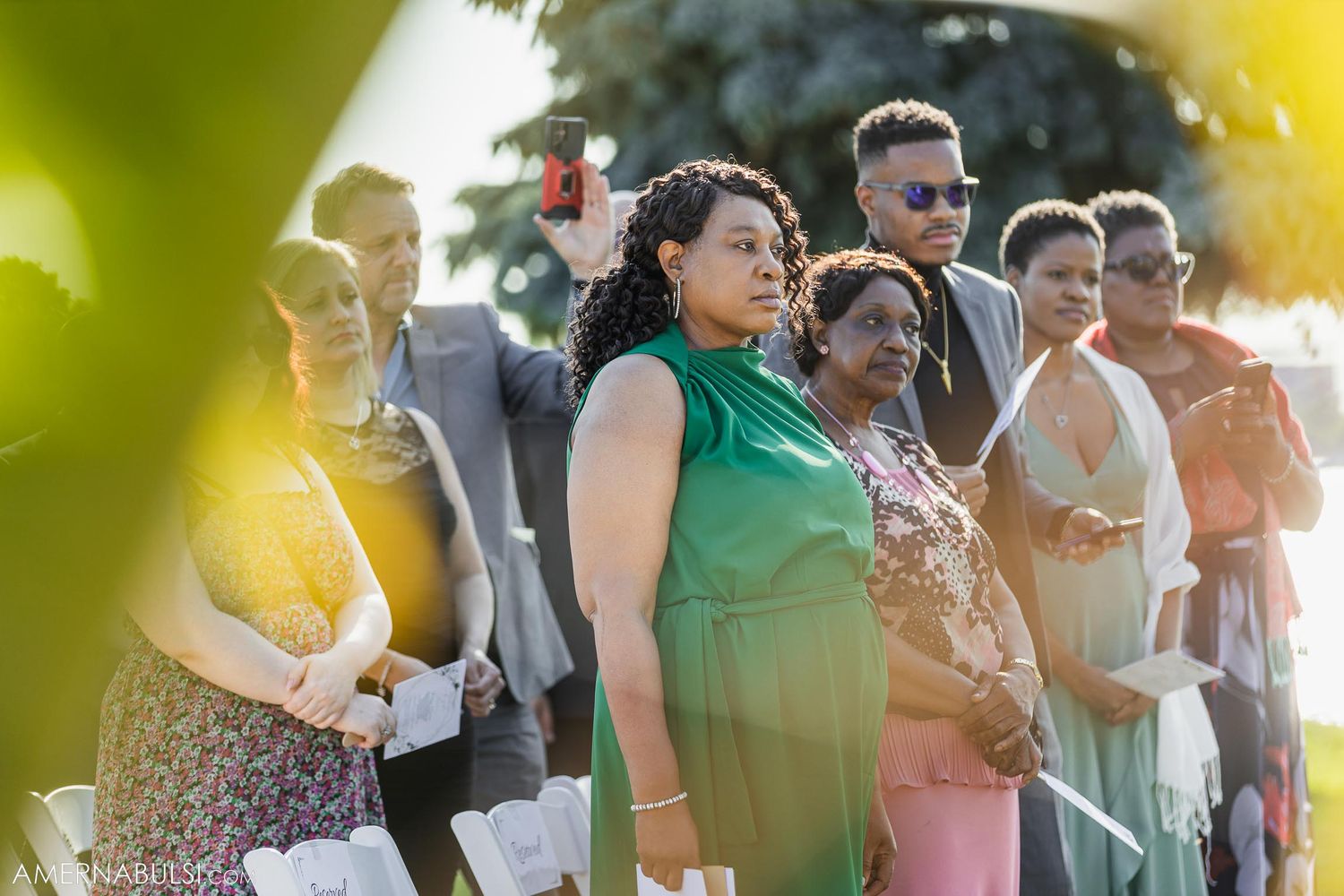Wedding guests in colorful attire gathered outdoors during summer ceremony.