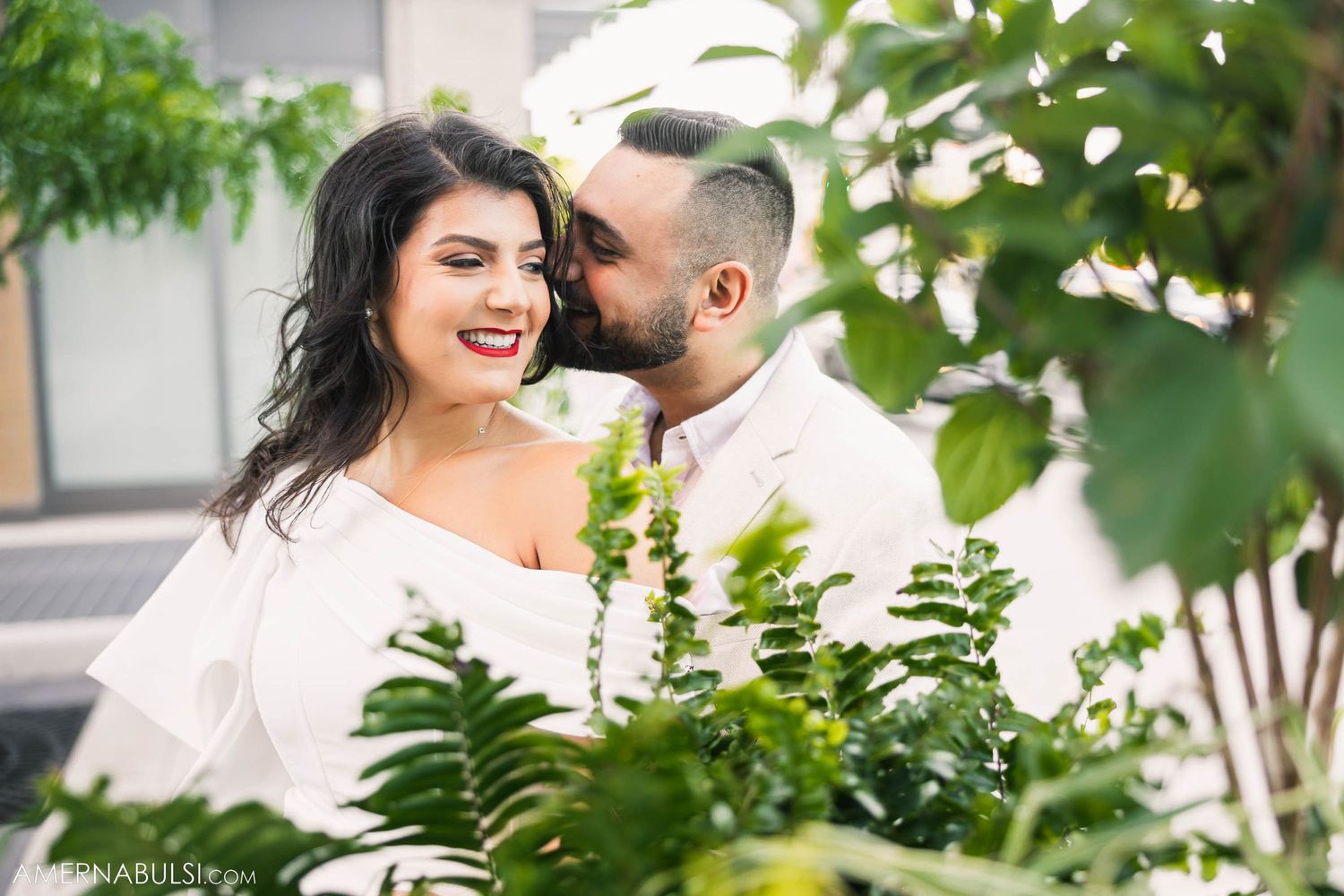 Romantic couple sharing intimate moment among tropical plants in outdoor setting.