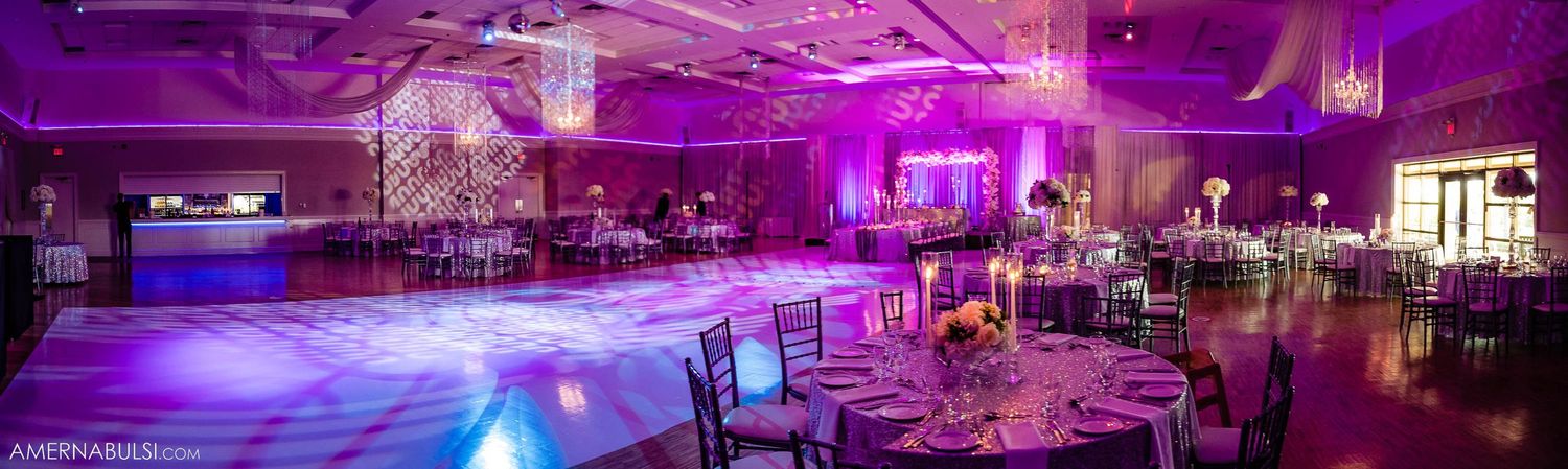 Panoramic view of a purple-lit wedding reception venue with elegant table settings and decor.