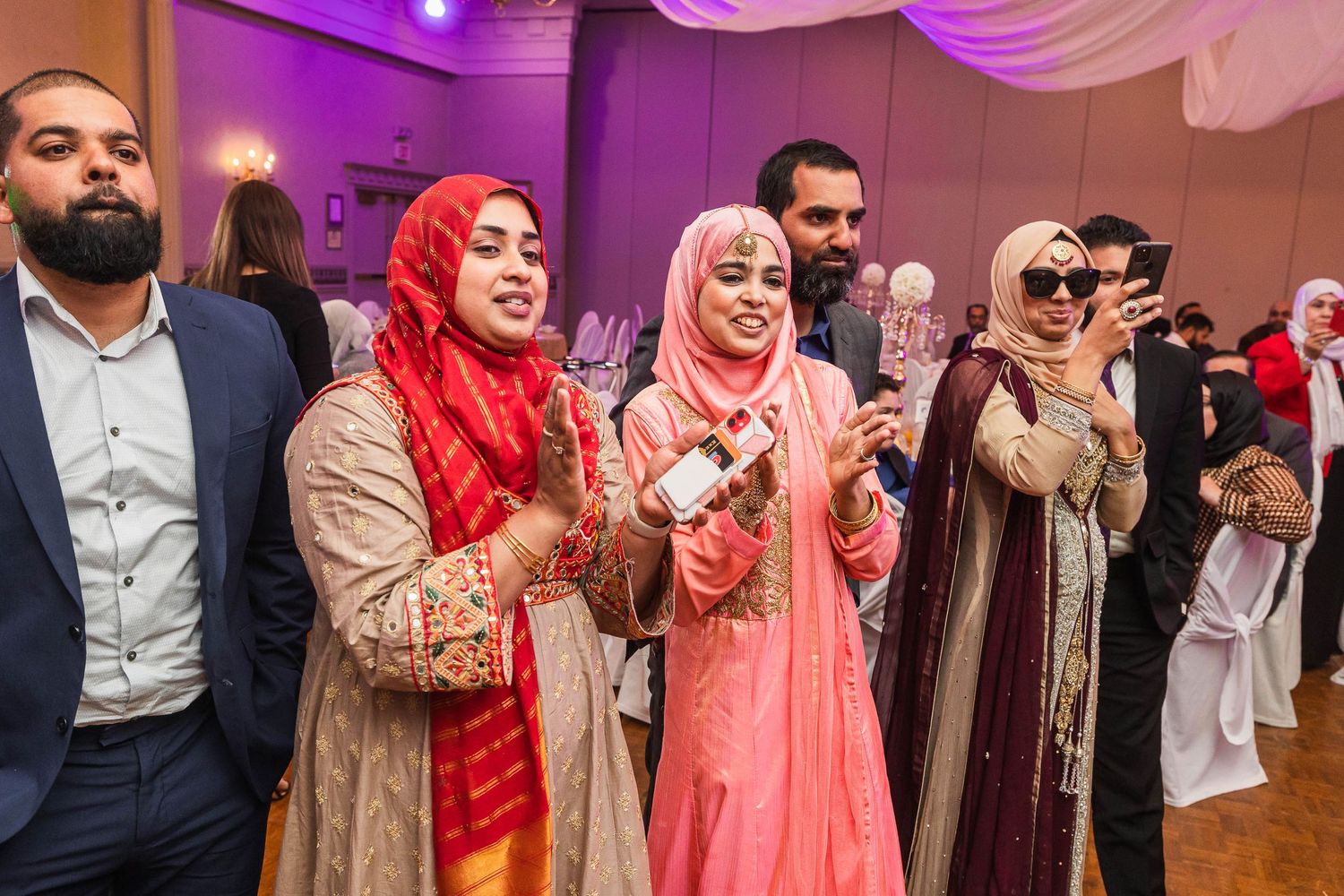 Wedding guests in formal attire capturing moments on their phones during the celebration.