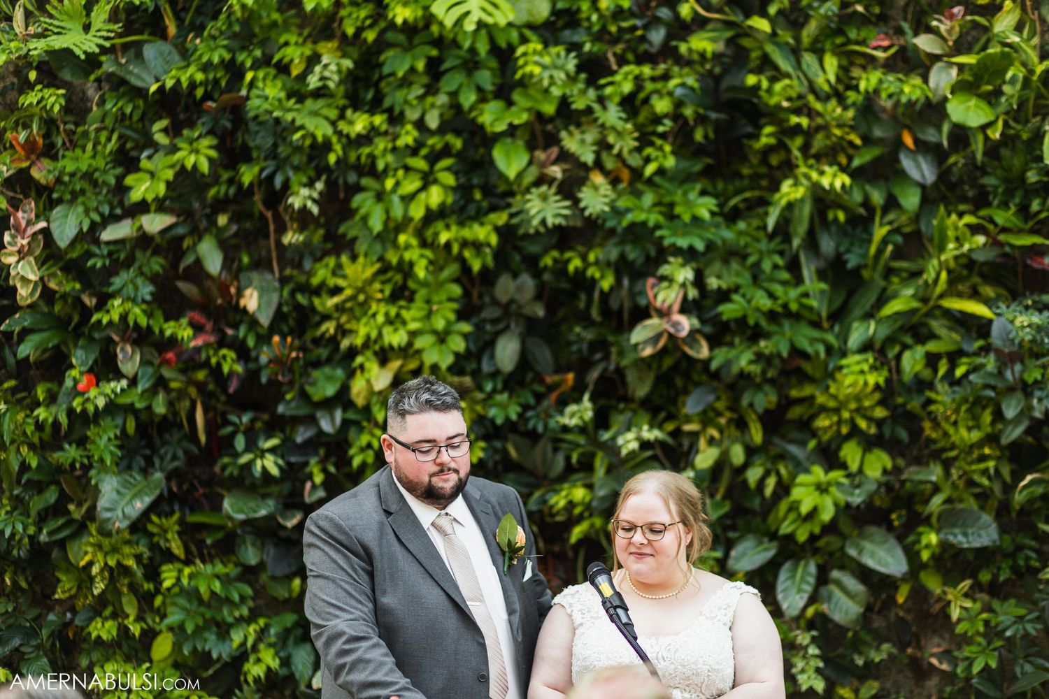 Newlyweds pose for portraits in front of a lush green garden wall.