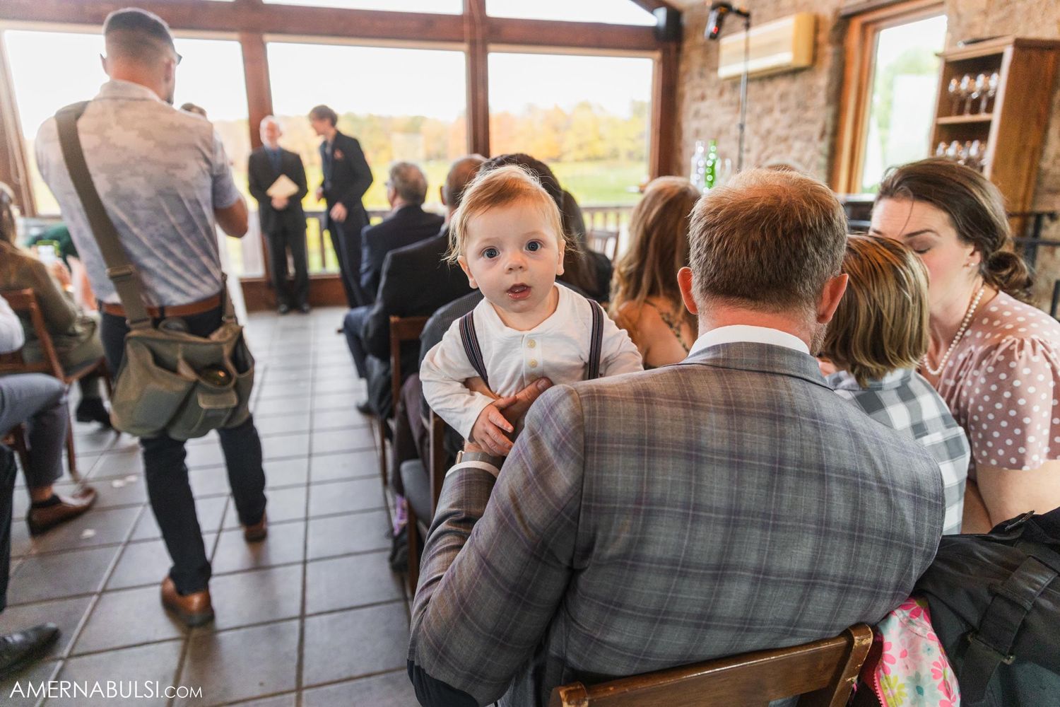 Wedding guests and a small child gather in chairs during an indoor reception.