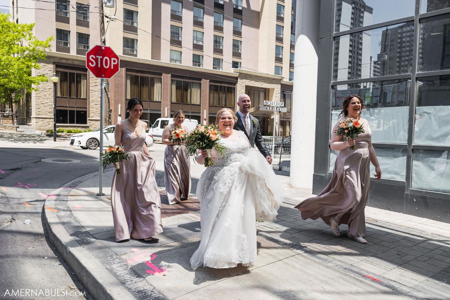 Wedding party dances and celebrates on city sidewalk near stop sign.
