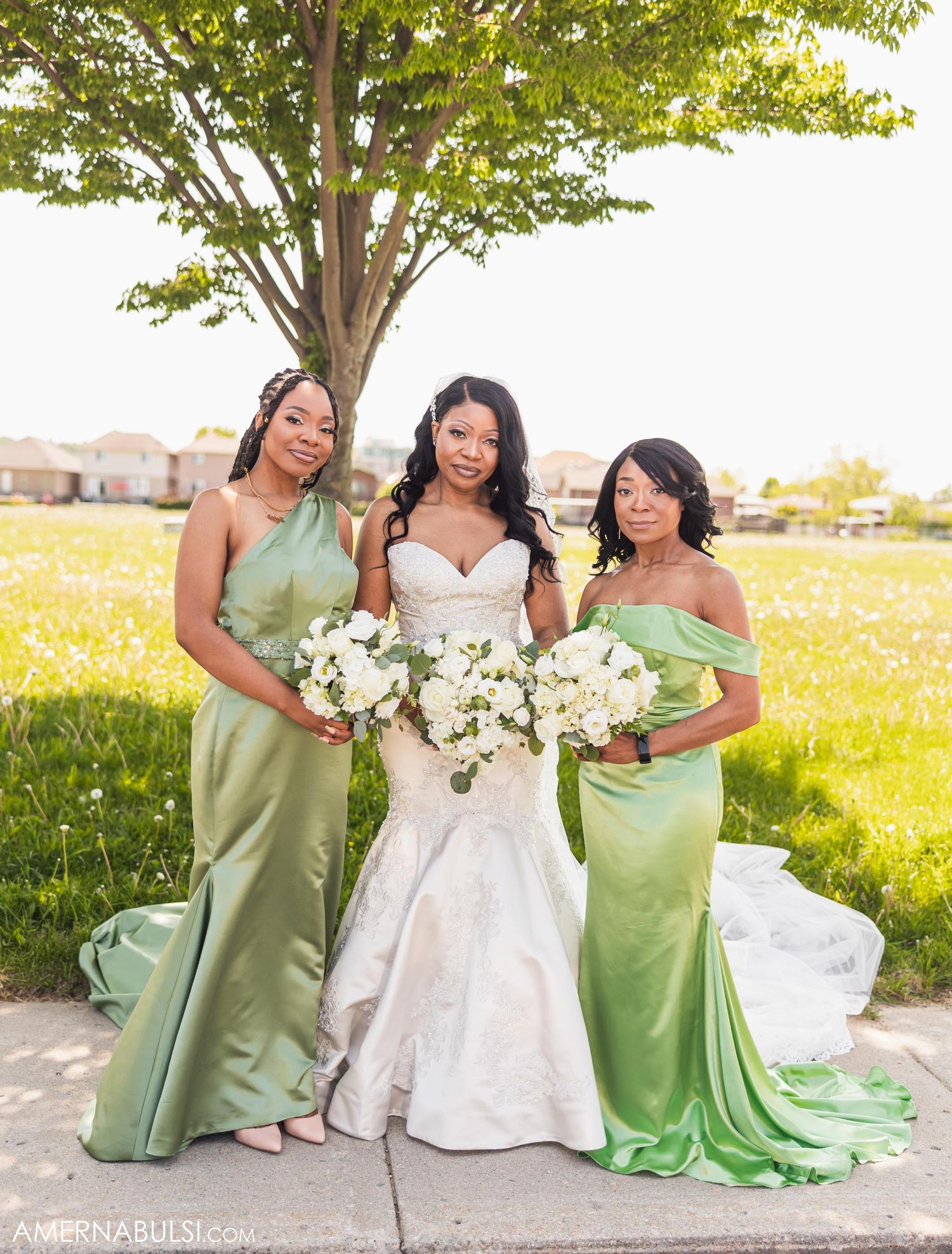 Bride in white gown poses with bridesmaids in matching sage green dresses holding bouquets.