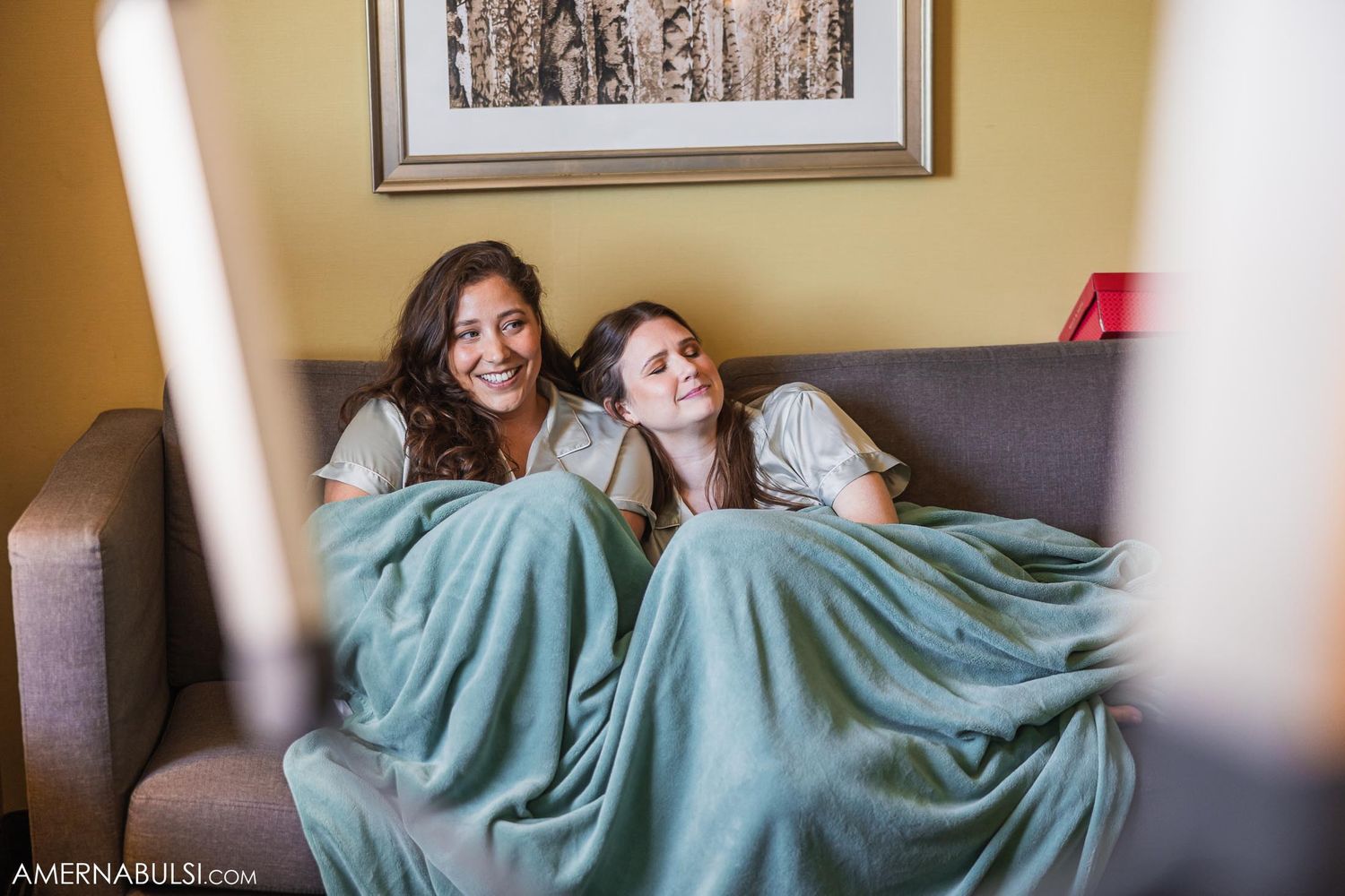 Two people relaxing under cozy blankets on a gray couch.