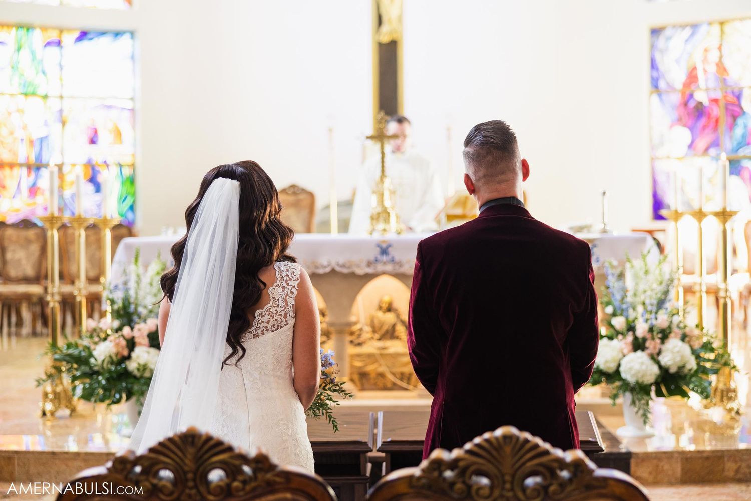 Couple standing at altar during wedding ceremony with stained glass windows in background.